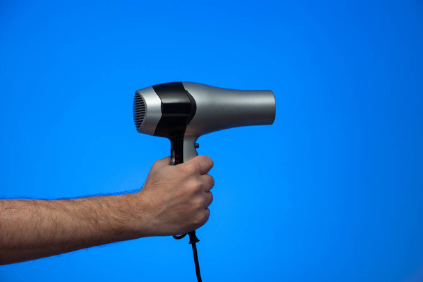 Caucasian male extended arm holding a hair dryer isolated on blue background studio shot. - Photo, Image