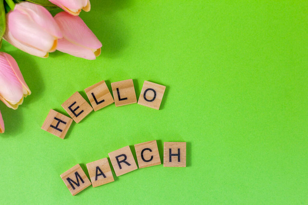 Hello, March.Wooden blocks with an inscription and tulips on a green background.The concept of the beginning of the long-awaited spring. - Photo, Image