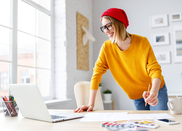 Щаслива молода жінка посміхається для ноутбука і пише в планувальнику, спираючись на стіл під час роботи над проектом вдома
 - Фото, зображення