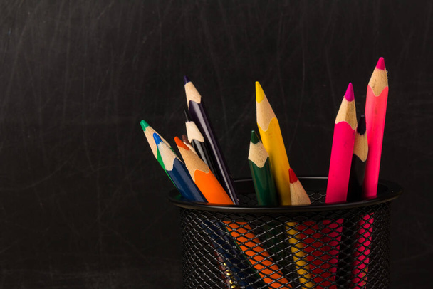 Crayons de couleur en support noir. Fournitures scolaires et de bureau sur la table de classe devant le tableau noir. Vue avec espace de copie - Photo, image