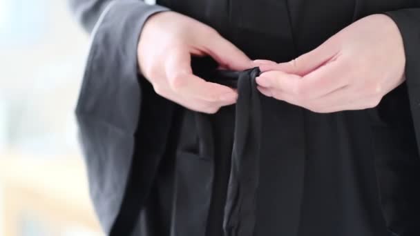 vrouw in zwarte zijden badjas bindt de riem om haar badjas. Van dichtbij gezien. Een slow motion video. voorraadbeelden - Video