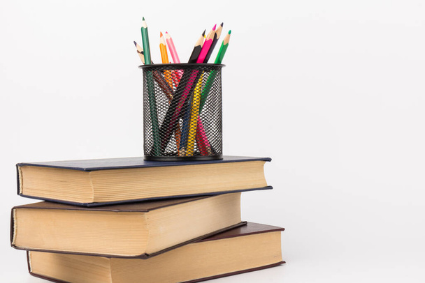 Színes ceruzák dróthálós csészében, könyvek fehér háttérrel, oktatás vagy vissza az iskolába koncepció - Fotó, kép