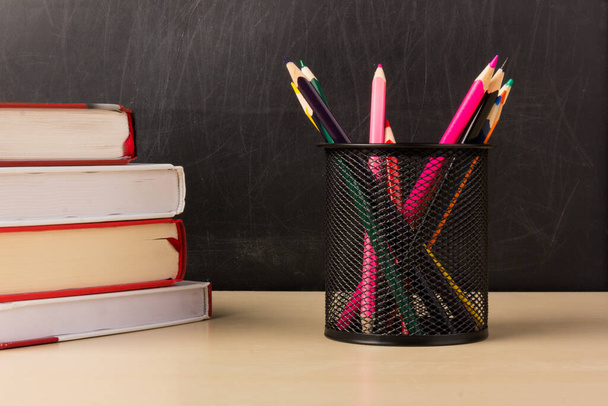 Lápices coloridos en taza de malla de alambre, libros en mesa de madera con pizarra en el fondo, educación o volver al concepto de la escuela - Foto, Imagen