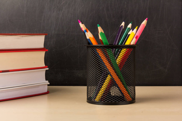 Színes ceruzák dróthálós csészében, fából készült asztali könyvek krétával háttal, oktatás vagy vissza az iskolába koncepció - Fotó, kép