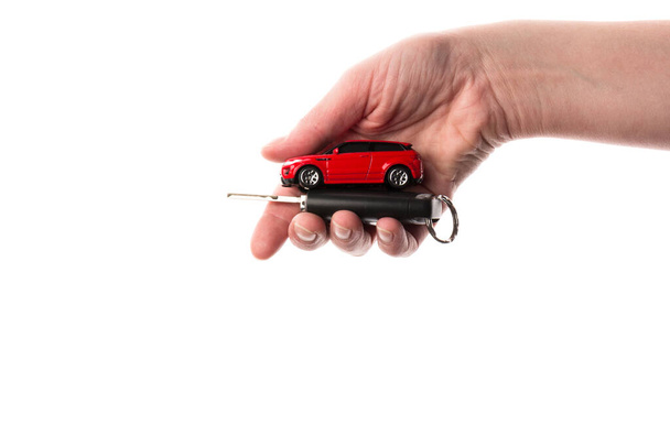 Рука держит ключи и красную игрушку автомобиля изолированы на белом. Концепция покупки автомобиля - Фото, изображение