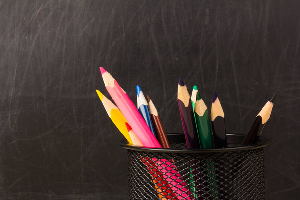 Χρωματιστά μολύβια σε μαύρη θήκη. Προμήθειες σχολείου και γραφείου στο τραπέζι της τάξης μπροστά από τον πίνακα. Προβολή με κενό αντιγραφής - Φωτογραφία, εικόνα