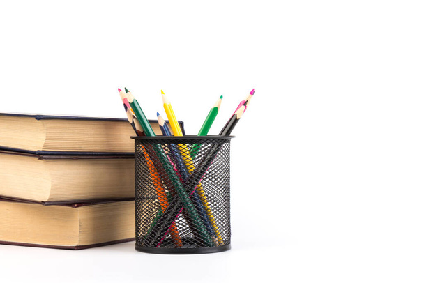 Kolorowe ołówki w drucianym kubku siatkowym, książki na białym tle, edukacja lub powrót do koncepcji szkoły - Zdjęcie, obraz