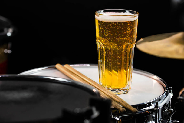 Ένα ποτήρι ελαφριά μπύρα με αλμυρά σνακ σε επαγγελματικό drum set closeup. Drumsticks, drums και cybals, σε live music rock συναυλία, σε club stage, bar, ή σε στούντιο ηχογράφησης. Μαύρο φόντο. - Φωτογραφία, εικόνα