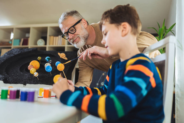 Happy school jongen en zijn vader het maken van een zonnestelsel voor een school wetenschap project thuis - Foto, afbeelding