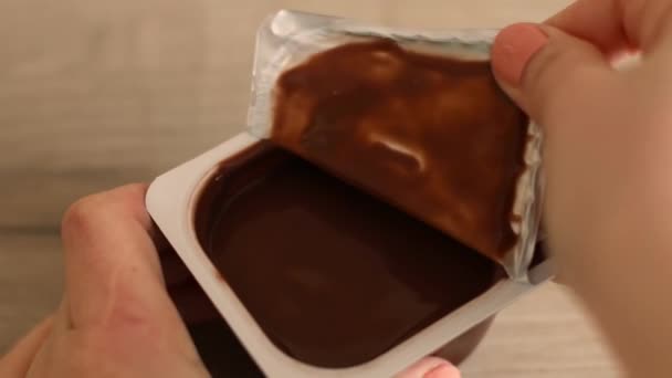 Man hand opens plastic container with chocolate mousse or pudding on wooden table - Footage, Video