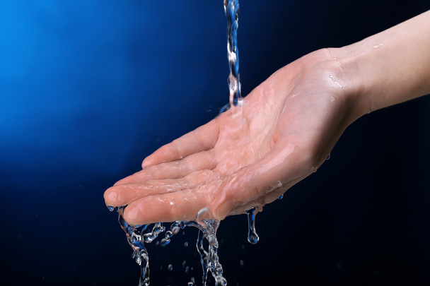 Human hand with water splashing on them on dark blue background - Фото, зображення
