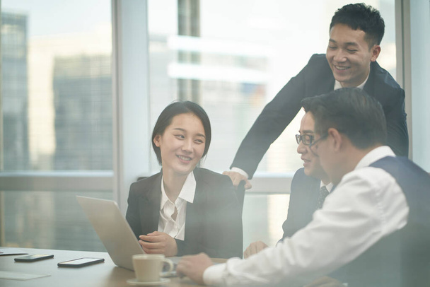 a través del vaso de un equipo de cuatro ejecutivos corporativos asiáticos reunidos en la oficina discutiendo negocios - Foto, imagen