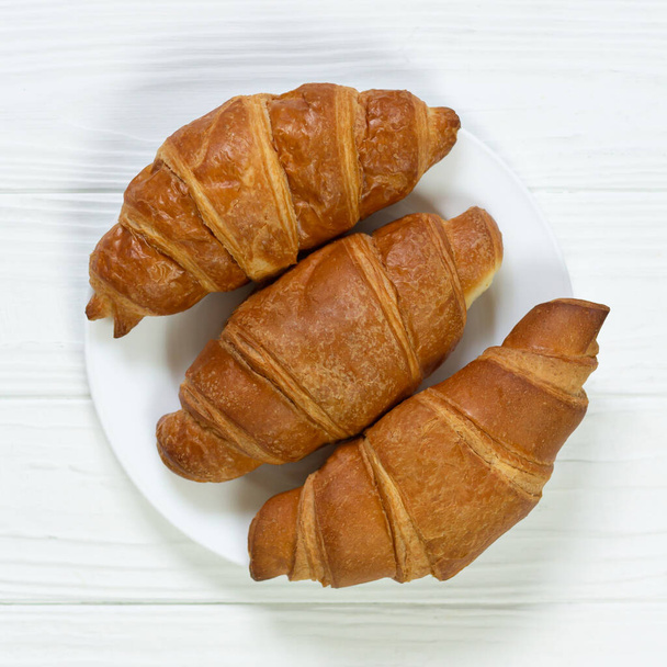 Teller mit frisch gebackenen Croissants auf weißem Holztisch - Foto, Bild