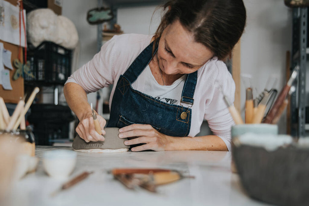 giovane donna artigianale che lavora con la mano un pezzo di ceramica messa a fuoco a portata di mano - Foto, immagini