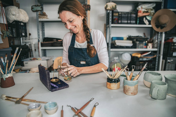 junge Kunsthandwerkerin bearbeitet mit ihren Händen ein Stück Keramik, das Farben mischt - Foto, Bild