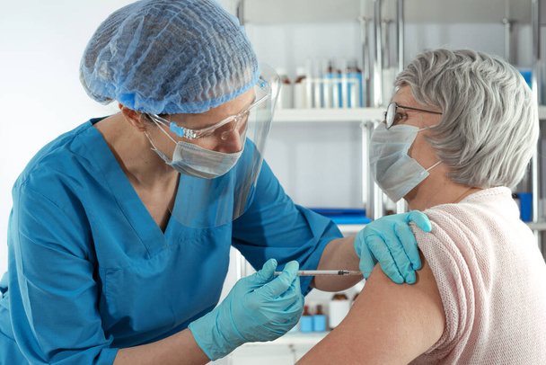 Naispuolinen lääkäri ruiskuttaa rokotetta aikuiselle naisvanhalle naiselle. Ulkouima sairaalan terveydenhuollon tapaus - Valokuva, kuva