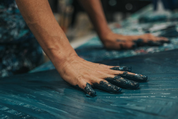 Jeune femme peint un tableau abstrait avec ses mains sur une table de travail dans son atelier intérieur. Focus sur la main - Photo, image