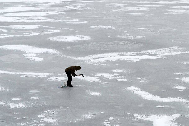 The man is chopping thin ice. Danger of winter fishing. - Photo, Image