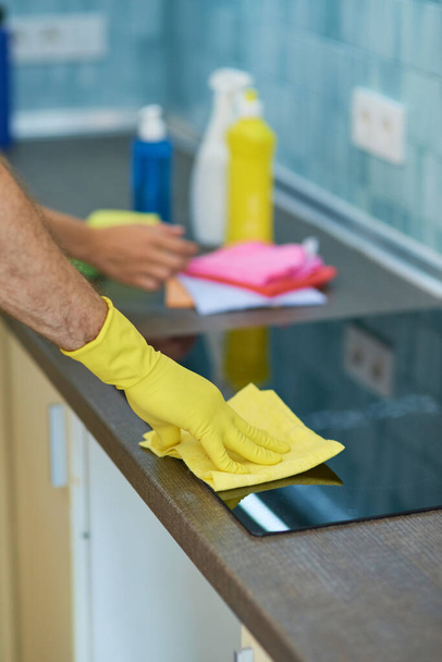Υπηρεσία δωματίου. Κοντινό πλάνο των χεριών του ανθρώπου, επαγγελματίας καθαριστής αρσενικών φορώντας γάντια, χρησιμοποιώντας απορρυπαντικά ενώ ο καθαρισμός φούρνου στην κουζίνα - Φωτογραφία, εικόνα