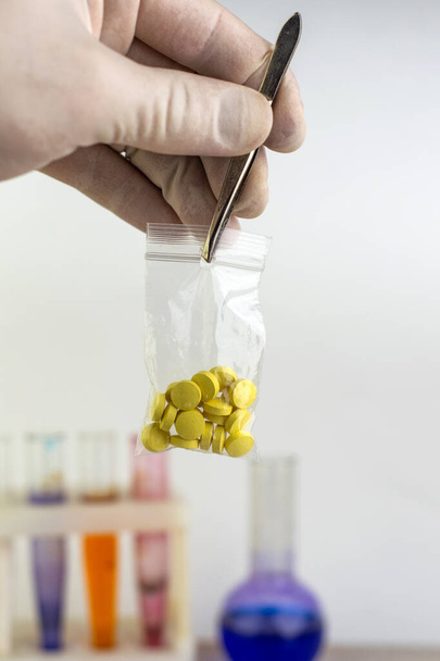 estudo de drogas sintéticas: um cientista detém uma amostra de uma nova droga acima da mesa com outras amostras, foco curto - Foto, Imagem