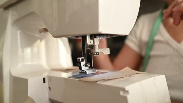 Camisa branca de costureira de mulher sênior confiante e óculos com máquina de costura, trabalhando em roupas em casa usando tecido bege. Pessoas aposentadas, idade, conceito de ocupação de emprego - Filmagem, Vídeo