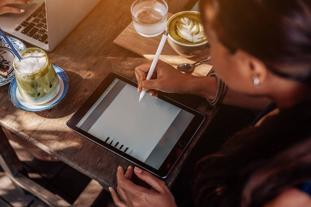 Aziatische vrouwelijke werknemer gebruikt haar tablet en pen zitten aan tafel buiten - Foto, afbeelding