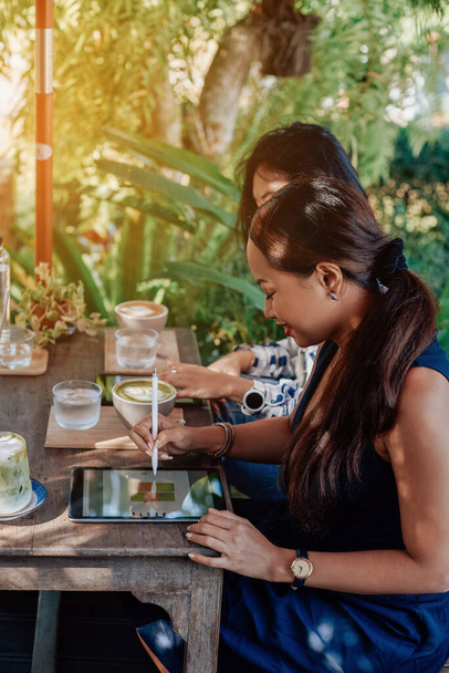 Fröhliche asiatische Frauen arbeiten mit modernen Tablets am Tisch draußen - Foto, Bild