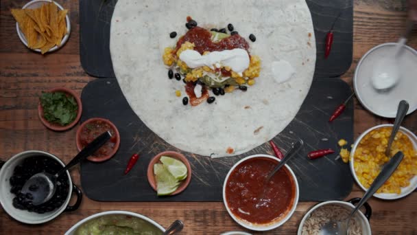 Overhead view of adding ingredients to tortilla and making a burrito. Top down view of adding fresh vegetables, sauces and herbs into tortilla and wrapping it up. Cutting burrito in half - Footage, Video