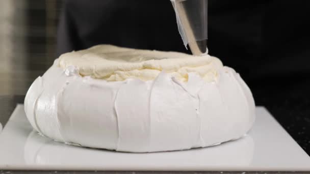 Pastelero llena brownies de crema con bolsa de pastelería. El proceso de hacer la torta Anna Pavlova. - Imágenes, Vídeo