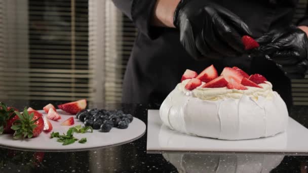 Chef pâtissier décore Anna Pavlovas gâteau avec des fruits frais et des feuilles de menthe. - Séquence, vidéo