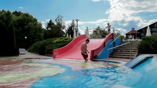 szczęśliwy chłopców na slajdzie w lecie basen - Materiał filmowy, wideo
