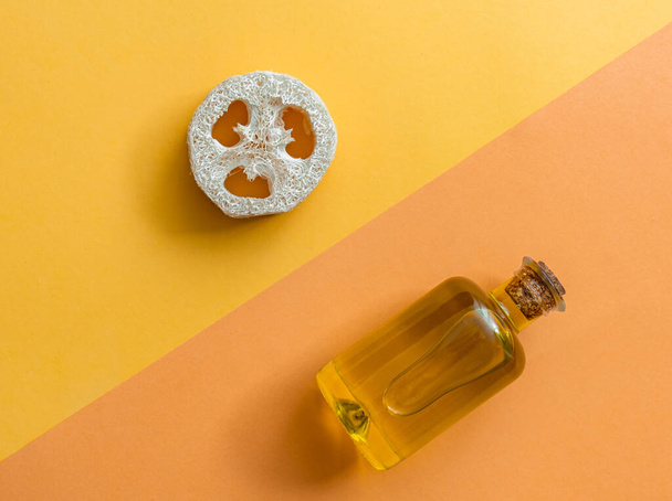 Μηδενικό προϊόν μπάνιου για οικιακή φροντίδα σε κίτρινο και πορτοκαλί γεωμετρικό φόντο.Σφουγγάρι και ελαιόλαδο Loofah σε γυάλινο μπουκάλι σε πολύχρωμο φόντοΟικολογικό, χωρίς πλαστική έννοια του βιώσιμου τρόπου ζωής - Φωτογραφία, εικόνα