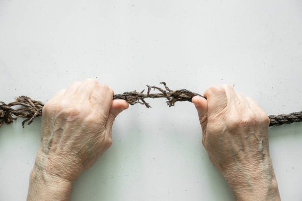 manos tiran de una cuerda vieja sobre un fondo blanco, fuerza humana - Foto, Imagen