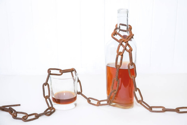 Old rusty chains around the bottle and glass. Addicted to alcohol. Dangerous habit. - Photo, Image