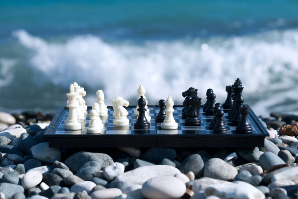 Шахматная доска с шахматистами во время шахматной игры на каменном пляже перед пенной волной - Фото, изображение