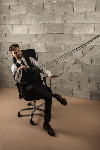 frightened, worried, pensive, man sitting on a chair, testing on a polygraph, wearing polygraph sensors, sitting on a gray brick wall background, wires held in his hands, holding hands, top view. - Photo, Image