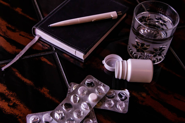 zelfmoord: een lege doos pillen naast een notitieblok, een glas water en blaren, toning - Foto, afbeelding