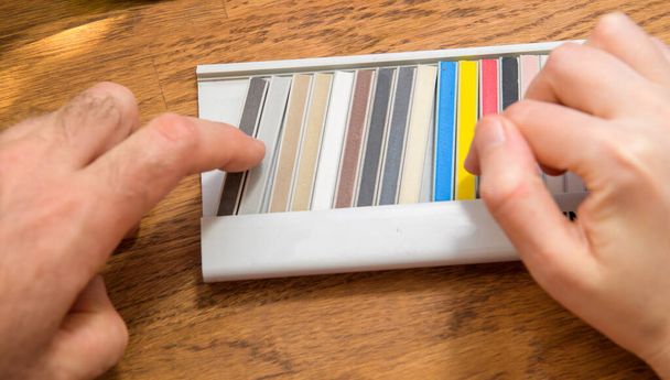 Vista aérea POV trabajador masculino mano elegir múltiples palos de muestra de colores con muestras de juntas de expansión en la mesa de madera - Foto, imagen