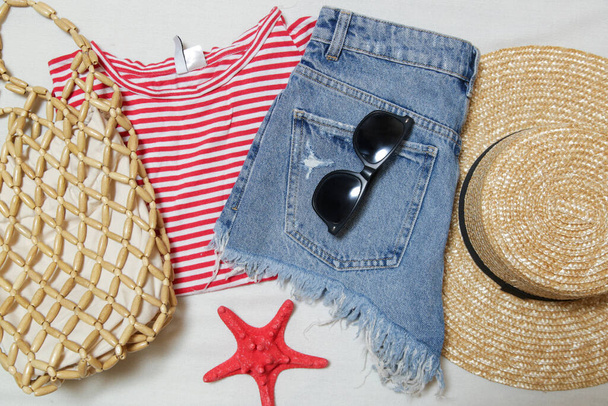 Simple summer outfit, denim shorts and striped cotton shirt with accessories on white background. Women's casual fashion items, top view. - Photo, Image