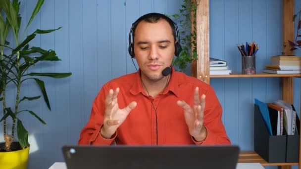 Młody mężczyzna w słuchawkach z mikrofonem prowadzącym rozmowę online - Materiał filmowy, wideo