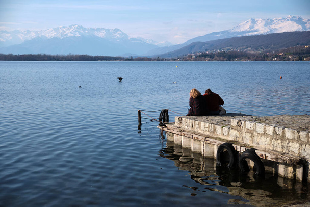 δύο άνθρωποι που κάθονται στην προβλήτα παρατηρούν το αλπικό πανόραμα από μια λίμνη - Φωτογραφία, εικόνα