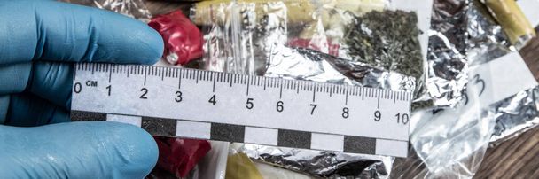 bewijs van smokkelhandel: forensische schaal in de hand van een deskundige tegen de achtergrond van drugspakketten - Foto, afbeelding