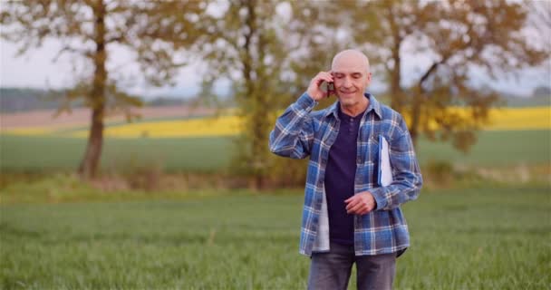 Agricultor hablando por teléfono móvil mientras trabaja en un campo de agricultura - Imágenes, Vídeo