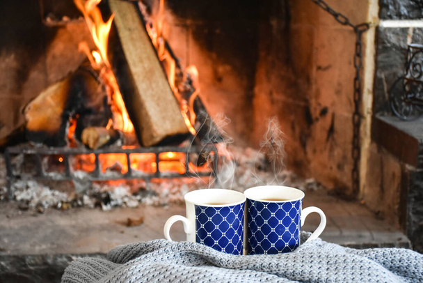 Two mugs (cup) of tea or coffee in front cozy and worm fireplace, in country house. Winter or autumn (fall) vacation.  - Photo, Image