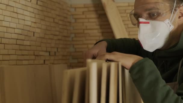 Trabajador de la madera profesional en máscara y gafas comprueba madera cruda, tablón de madera, panel de madera contrachapada - Metraje, vídeo