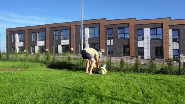 Hombre caucásico enseñar pequeño hijo cortar hierba en el jardín con cortacésped de juguete. Movimiento del cardán - Metraje, vídeo