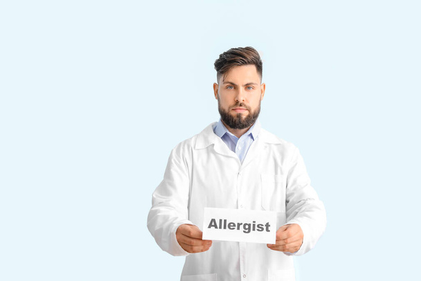 Doctor sosteniendo papel con palabra ALERGISTA sobre fondo de color - Foto, Imagen