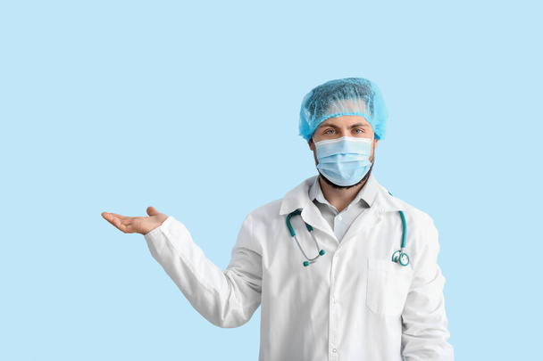 Arzt in medizinischer Maske zeigt etwas auf farbigem Hintergrund - Foto, Bild