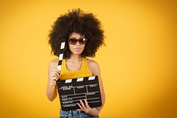 Fiatal, mosolygós afro-amerikai nő alkalmi nadrágban, sárga-narancssárga háttérrel. Az emberek életmód koncepciója. Másolás. Tartsd fel a klasszikus fekete papírlapot. - Fotó, kép