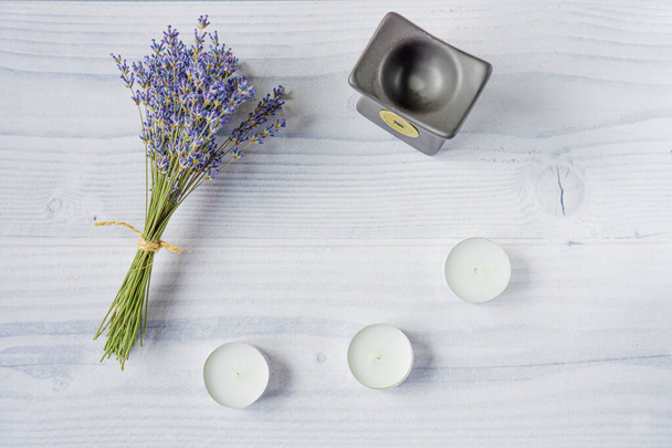 Schöner Strauß frischer Lavendelblüten liegt auf hellem Holztisch neben schwarzer Keramik-Duftlampe und weißen Teelichtern. Konzept der Aromatherapie, Entspannung zu Hause, Wellness-Behandlungen. Flache Lage, Draufsicht - Foto, Bild